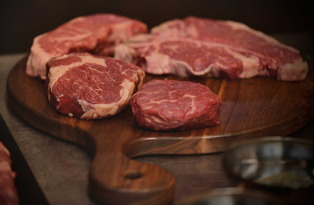 Herd & Grace raw marbled beef steaks on a wooden cutting board