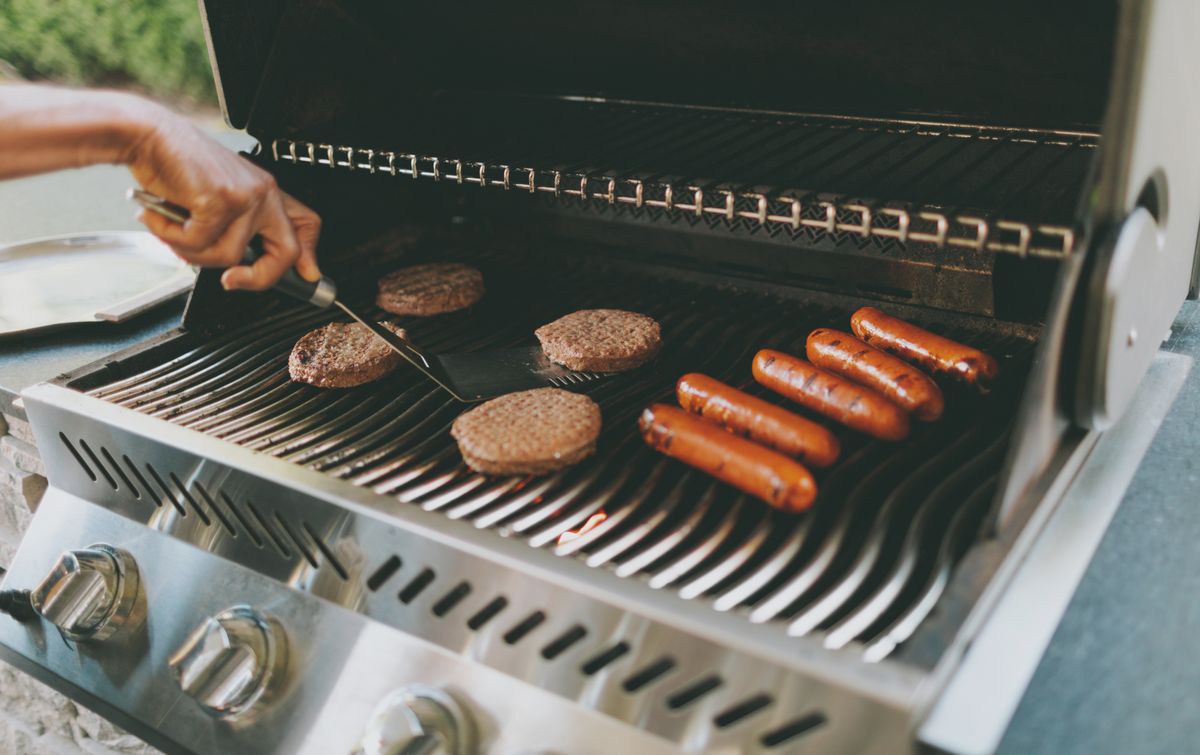Person grilling burgers and sausages on a barbecue