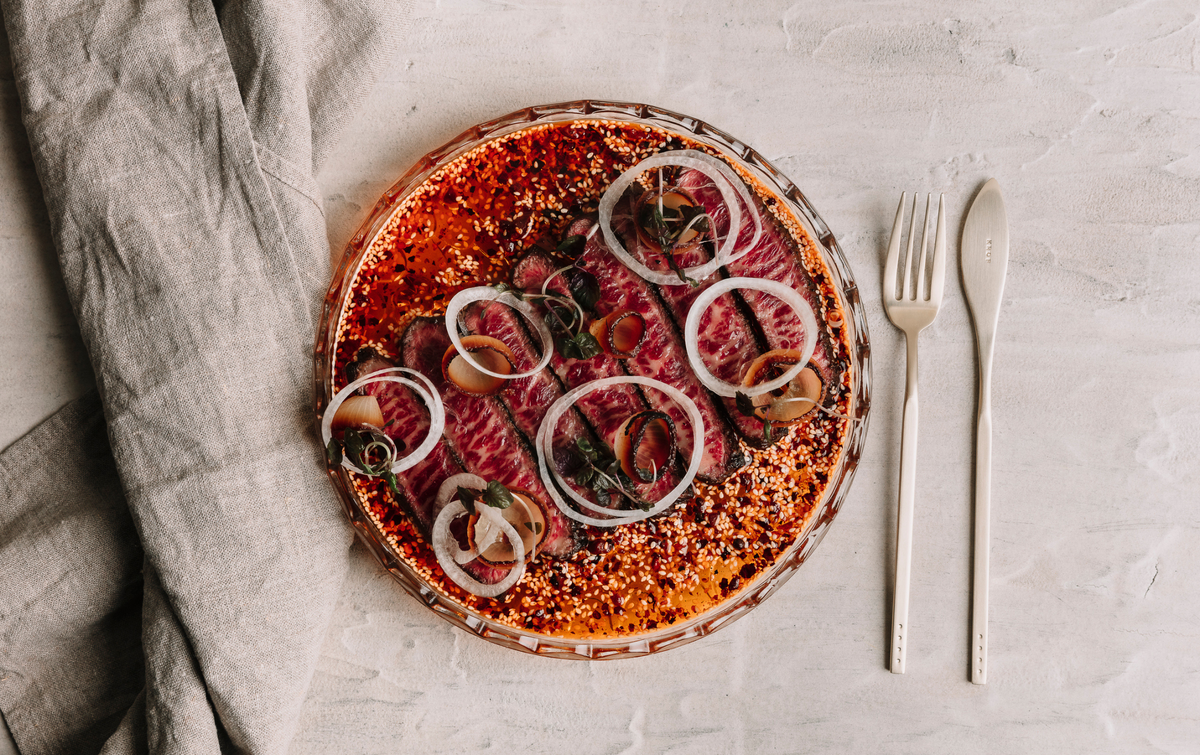 Raw pizza with onions and herbs on a stone surface with a fork and knife.