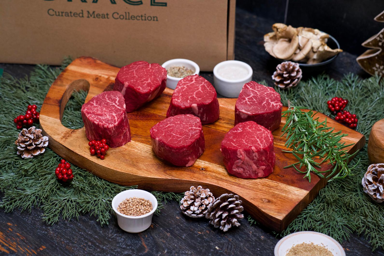 Six raw filet mignon steaks on a wooden board with a Herd & Grace box